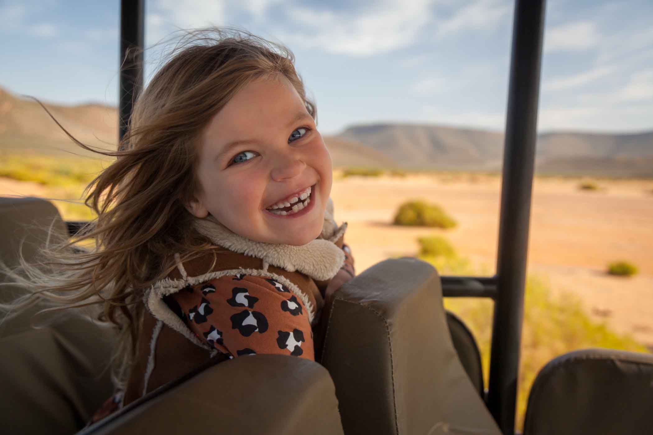 young girl sitting in the back of a safari vehicle and smiling. Read Aquila's children policy for more info.