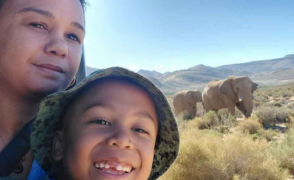 A mother and her son on a safari vehicle looking at elephants grazing nearby  at Aquila Private Game Reserve: Should you take your children on safari with you?