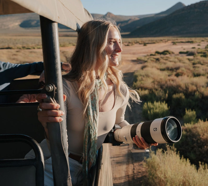 Karlie Place, a USA-based social media and adventure travel writer, leaning out of an open-air safari vehicle with her camera at Aquila Private Game Reserve and Spa: Big 5 Safari only 2 hours from Cape Town